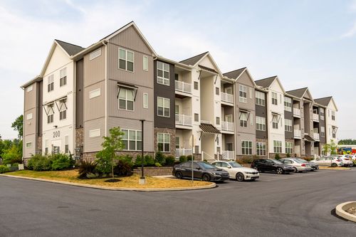 Street-level view of a gray and tan apartment building with parked cars along the curb