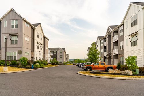 Street-level view of an apartment courtyard drive with an orange pickup truck parked between buildings