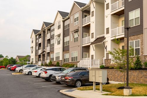 Street-level view of a row of apartment buildings with cars parked along the curb