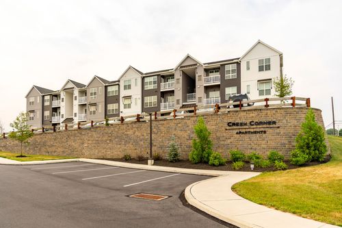 Stone entrance wall for Creek Corner Apartments with a building and landscaping behind