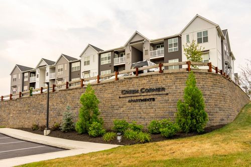 Close-up of the Creek Corner Apartments stone entrance sign framed by evergreen shrubs