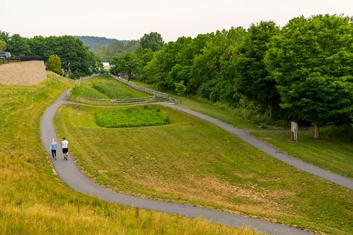 Two joggers on a paved trail through a grassy community park lined with trees