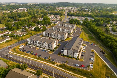 Aerial view of an apartment community along a tree-lined road with rolling farmland in the distance