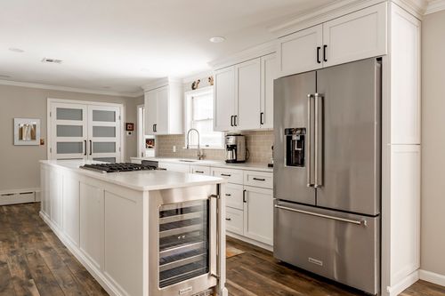 White kitchen island with black hardware, a wine cooler and a stainless steel refrigerator