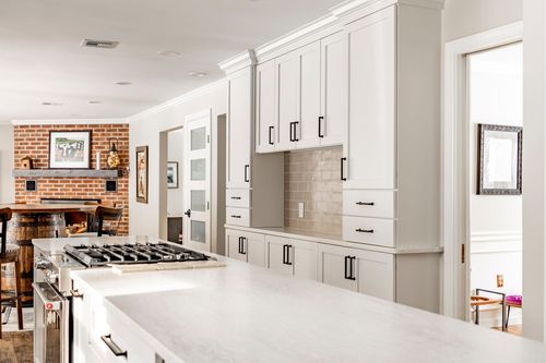 White kitchen with subway tile backsplash, gas cooktop and a brick fireplace visible beyond