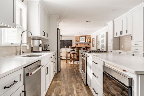 Open kitchen and living space with a stainless gas range, white cabinets and a brick fireplace