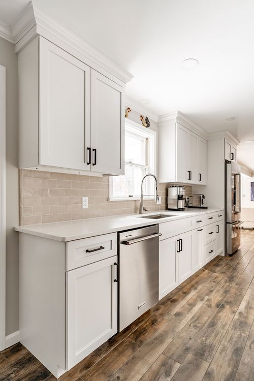 White kitchen with subway tile backsplash, wood flooring and a stainless dishwasher