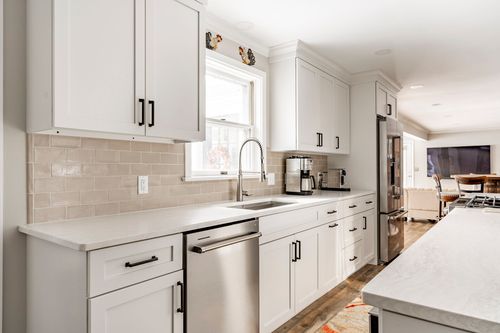 Kitchen sink area with subway tile backsplash opening to a living room with a wall-mounted TV