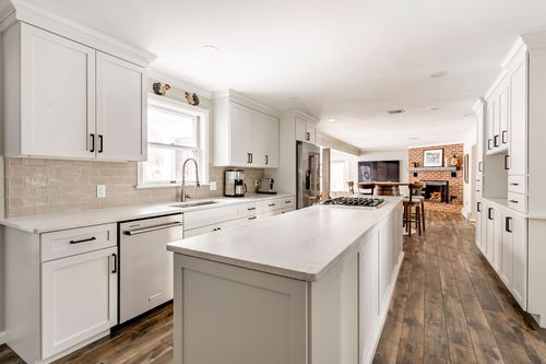 Open-concept kitchen and living room with a white island, wood floors and a brick fireplace