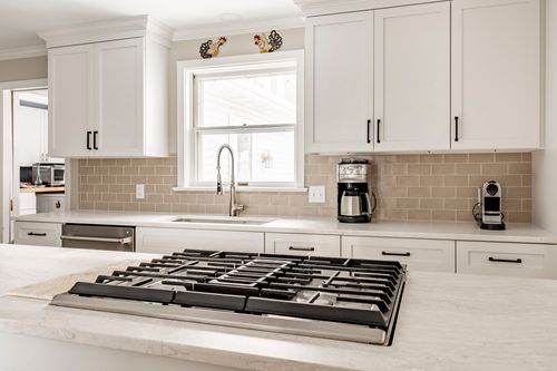 Close-up of a stainless gas cooktop with subway tile backsplash and coffee makers on the counter
