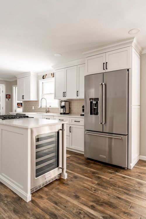 Stainless refrigerator and built-in wine cooler in a white kitchen with wood flooring