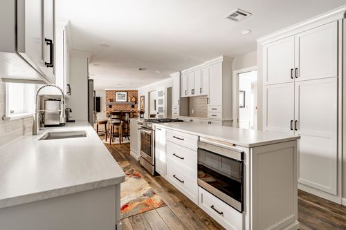 Long white kitchen with a stainless gas range, black hardware and a runner rug on wood floors