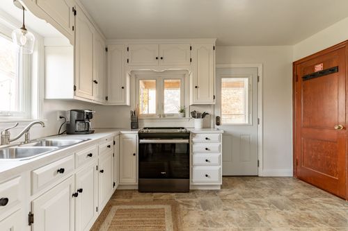 White kitchen with a garden window, black hardware and a paneled red back door