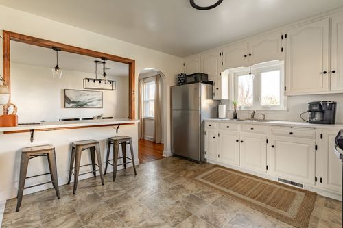 Breakfast bar with metal stools overlooking a white kitchen with a stainless fridge
