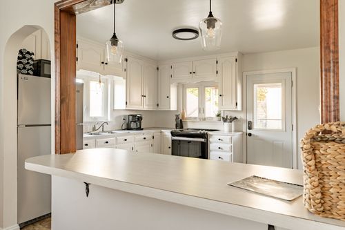 View through a wood-framed archway into a white kitchen with stainless appliances and a wicker basket