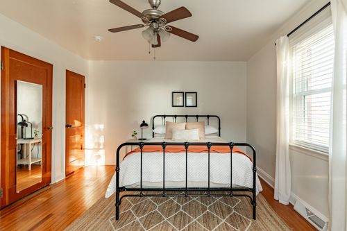 Bedroom with a black iron bed frame, ceiling fan and an orange throw over neutral bedding