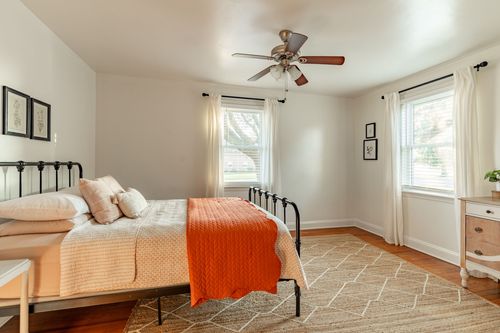Bedroom with a black metal bed, orange throw blanket, ceiling fan and a jute area rug