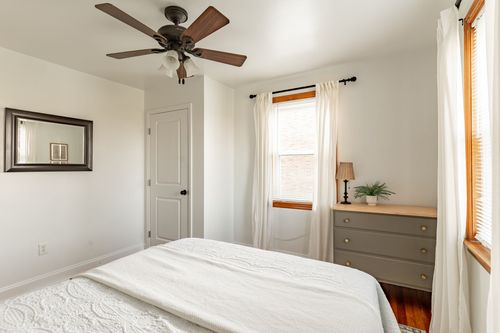 Bedroom with a wood-blade ceiling fan, white bedding and a gray dresser with brass pulls