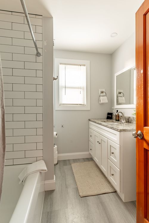 Bathroom with white subway-tile shower, granite vanity top and a wood-stained door