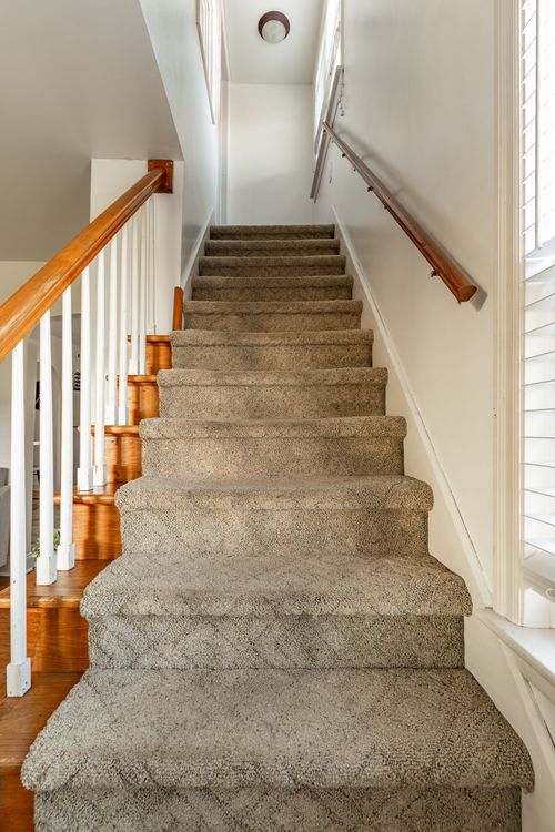 Staircase with a patterned carpet runner, wood banister and hardwood landing