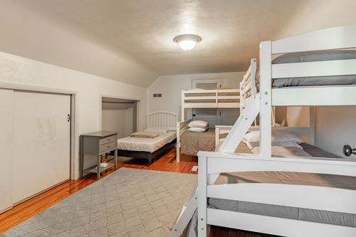 Bedroom with white bunk beds, a single bed and hardwood floors under a sloped ceiling