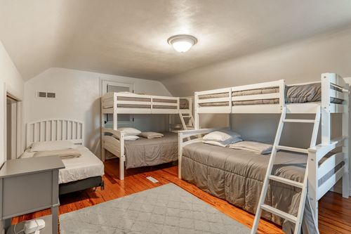 Bedroom with two white bunk beds, gray bedding and a patterned area rug