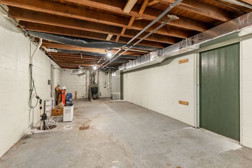Unfinished basement with exposed wood joists, block walls and a green door