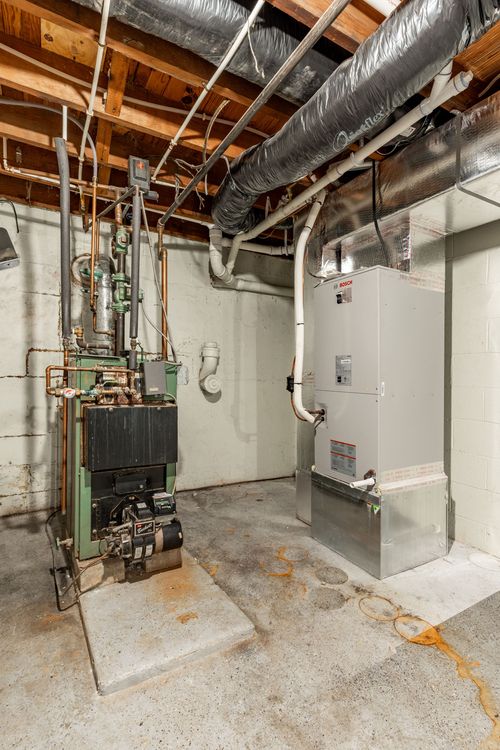 Basement mechanical room with a green boiler and gray HVAC air handler