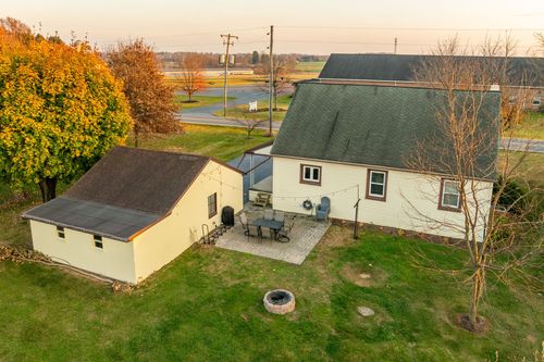 Aerial view of a cape-style home with a patio, fire pit and detached garage at dusk