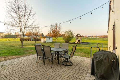 Backyard patio with string lights, a dining set and playset overlooking open fields