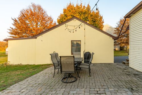 Backyard patio with a dining set beside a cream stucco outbuilding under string lights