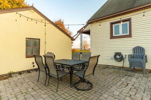 Patio with a dining table and blue Adirondack chairs beside matching cream buildings