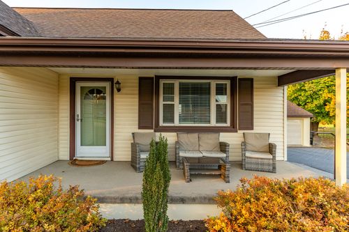 Covered front porch with wicker seating, a coffee table and autumn shrubs by the entry