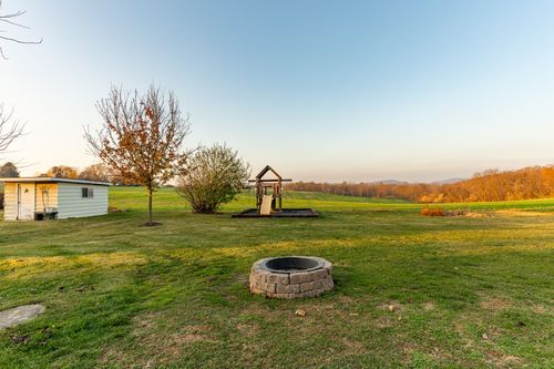 Backyard fire pit and wooden playset set in a wide open lawn at sunset