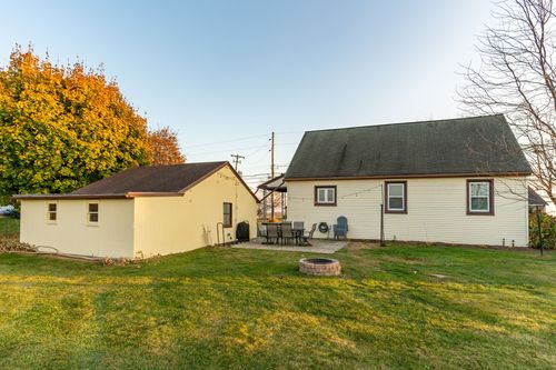 Rear exterior of a cream farmhouse with patio seating and a fire pit