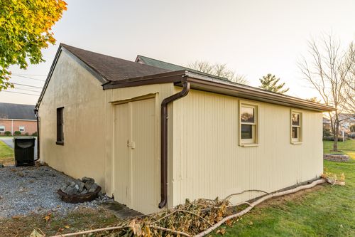 Side exterior of a cream outbuilding with gutters and a stone walkway