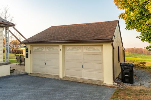 Detached two-car garage with cream siding and a brown shingle roof