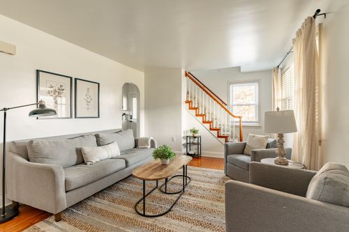 Living room with gray sofas, a bright orange stair railing and a jute area rug