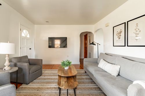 Living room with gray sofas, a wall-mounted TV and an arched doorway to the kitchen