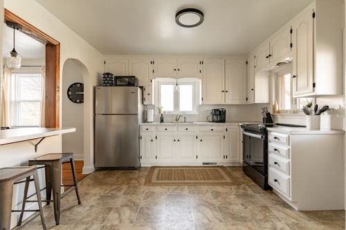 White kitchen with a stainless refrigerator, black hardware and tile flooring