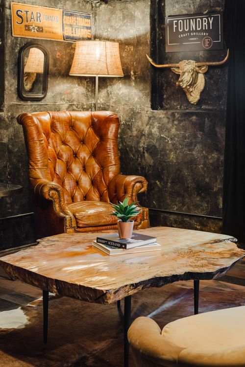 Tufted leather wingback chair beneath vintage tin signs and a gold longhorn head