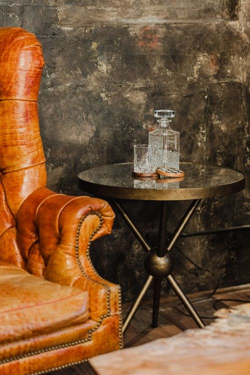 Crystal decanter and glasses on a round brass side table beside a leather chair