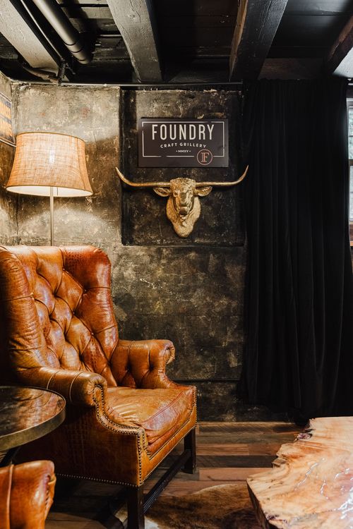 Tufted leather chair beneath a gold longhorn sign against a dark textured wall