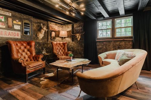 Den with leather wingback chairs, a curved velvet sofa and black-curtained windows