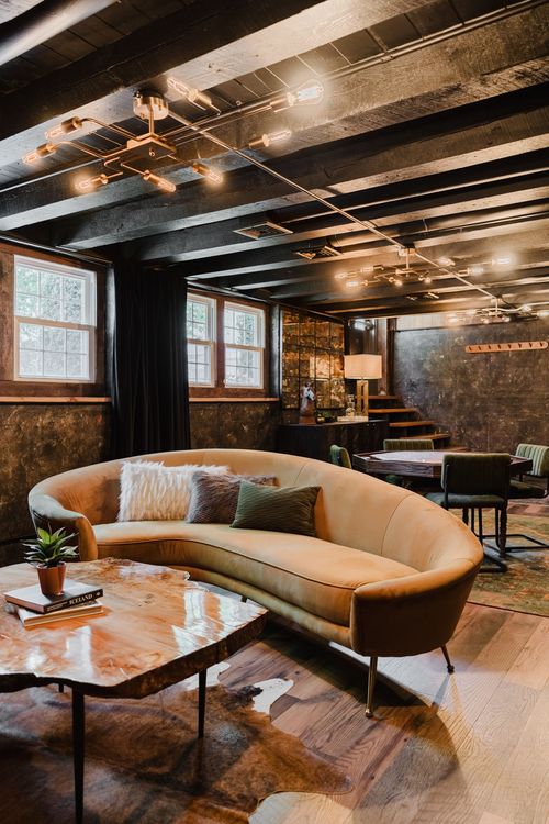 Curved sofa and an octagonal poker table in a black-beamed basement lounge