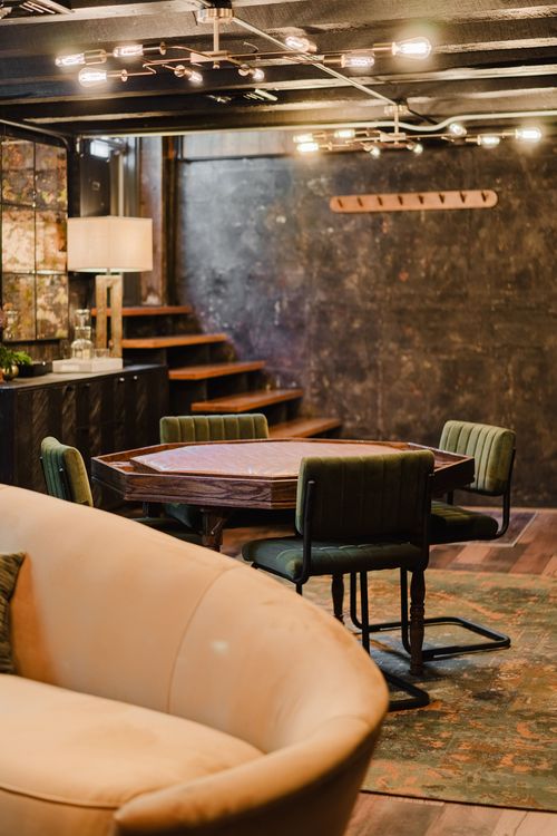 Octagonal leather-top poker table with green channel-tufted chairs beneath open stairs