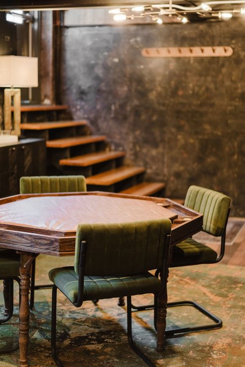 Green velvet chairs around an octagonal card table beneath an open wood staircase