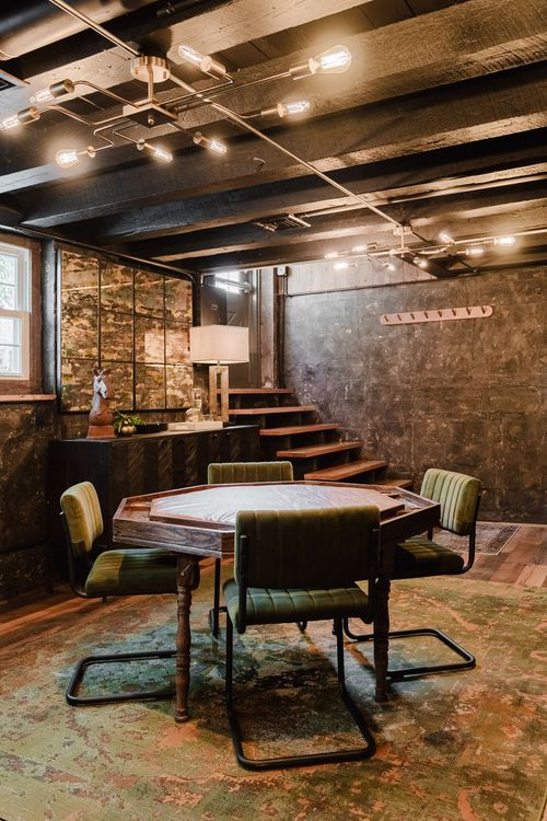 Game room with a poker table, green velvet chairs and an open wood staircase