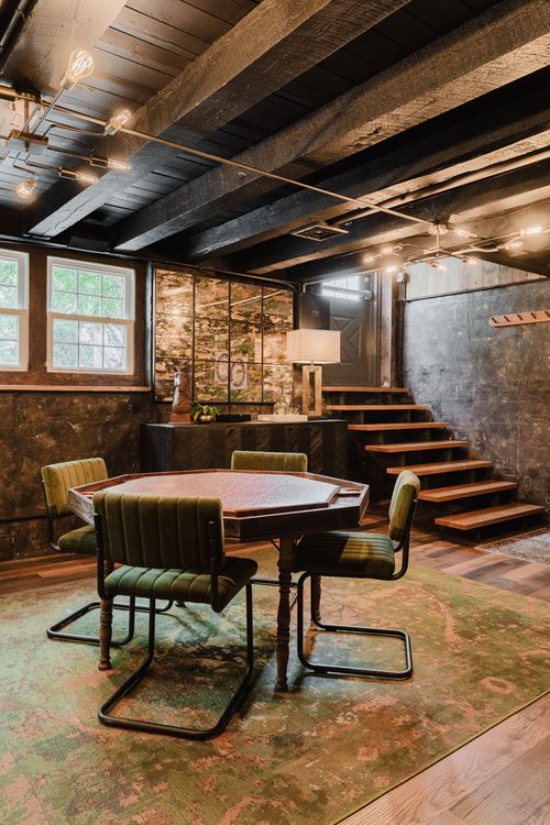 Octagonal poker table with green velvet chairs beneath a beamed ceiling and stairs