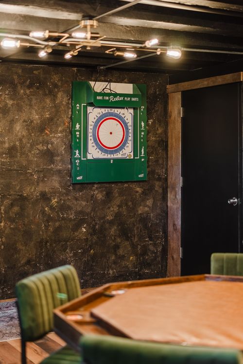 Vintage green dartboard mounted on a textured wall above a poker table
